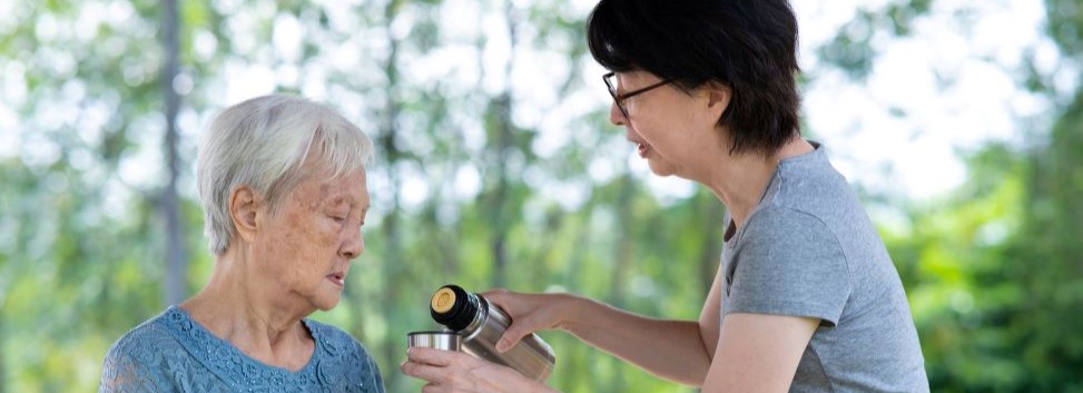 Older person getting hydration from caretaker outdoors